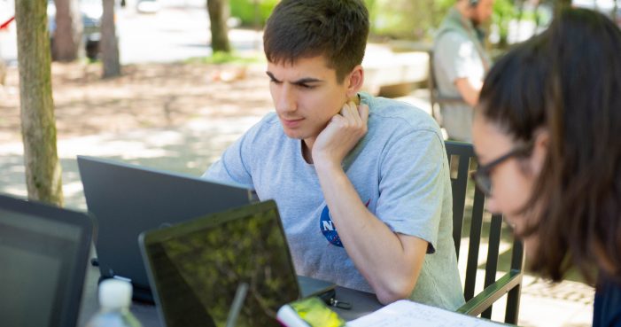 Two students on laptops outside